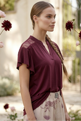 Woman wearing a burgundy blouse with floral details in an outdoor setting