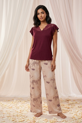 Woman wearing a burgundy top and patterned pants standing in front of draped curtains.