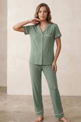 Woman wearing a green pajama set with white piping in a minimalistic room.