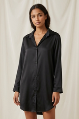 Woman wearing a black shirt dress against a white curtain background