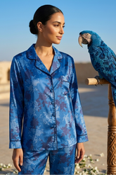 Woman in blue pajama set with a parrot on a wooden perch outdoors.