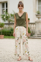 Woman wearing a green sleeveless top and floral pants standing in front of a building.