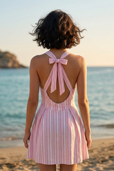 Woman wearing a pink striped dress with a bow back on a beach at sunset.