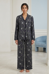 Woman wearing a black patterned pajama set in a room with light blue walls and a white floor.