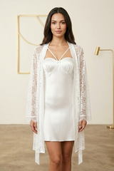 Woman wearing a white satin nightgown with a lace cover-up in a minimalistic room.