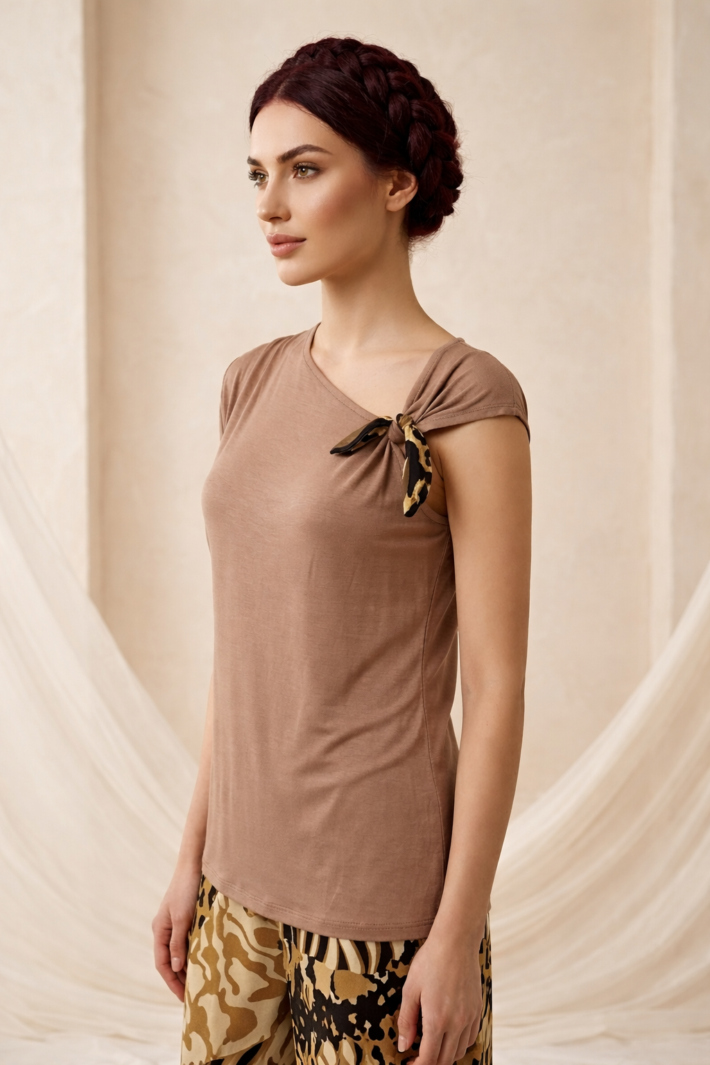 Woman wearing a brown top with a bow detail against a beige curtain background