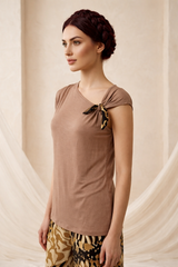 Woman wearing a brown top with a bow detail against a beige curtain background