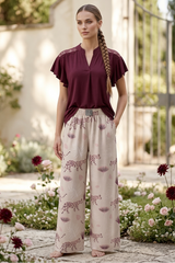 Woman in a burgundy top and patterned pants standing in a garden.