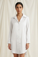 Woman wearing a white shirt dress against a plain background