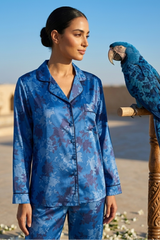 Woman in blue pajama set with a parrot on a wooden perch outdoors.
