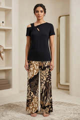 Woman wearing a black top and patterned pants standing in a room with shelves and a mirror.