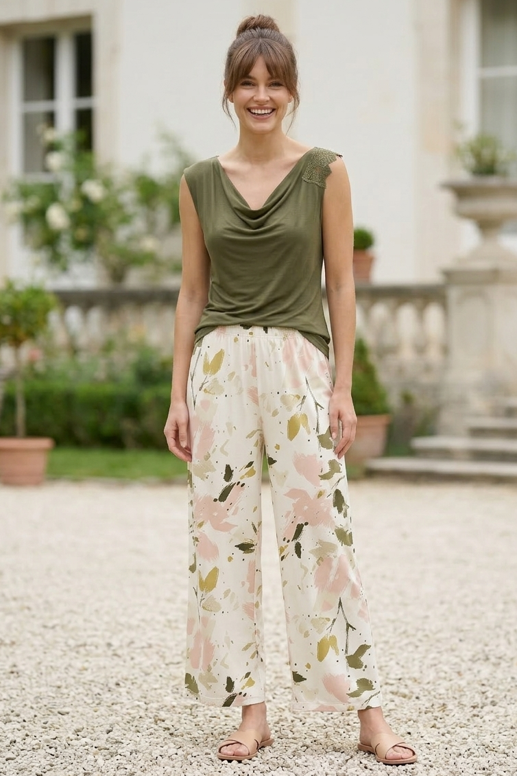 Woman wearing a green sleeveless top and floral pants standing in front of a building.