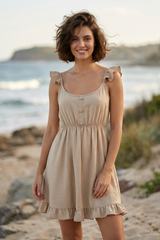 Woman in a beige dress standing on a beach with ocean and cliffs in the background