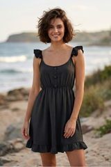 Woman in a black dress standing on a beach with ocean in the background