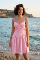 Woman in a pink dress standing on a beach with ocean and cliffs in the background