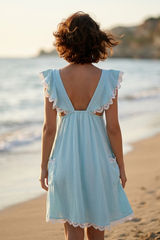 Woman in a light blue dress with lace details standing on a beach.