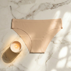 Beige bikini bottom on a marble surface with a candle